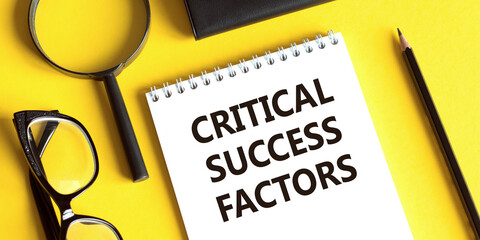 Notepad with the text CRITICAL SUCCESS FACTORS on a yellow background with glasses, a magnifying...