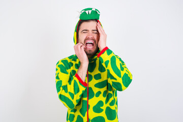 Doleful desperate crying young caucasian man wearing a pajama standing against white background, looks stressfully, frowns face, feels lonely and anxious