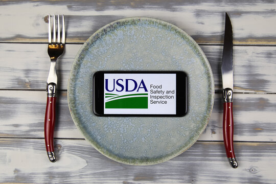 Viersen, Germany - February 9. 2021: Closeup of smartphone screen with logo lettering of usda food safety inspection service on plate with cutlery