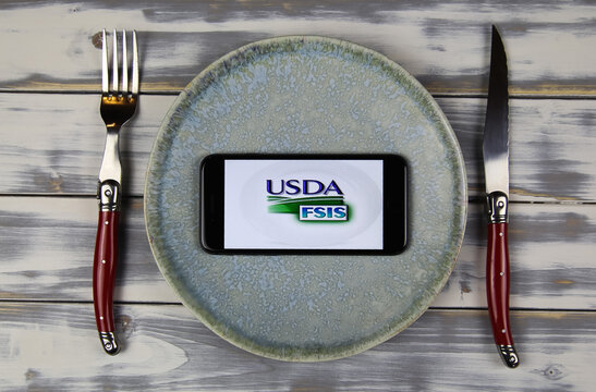 Viersen, Germany - February 9. 2021: Closeup Of Smartphone Screen With Logo Lettering Of Usda Food Safety Inspection Service On Plate With Cutlery