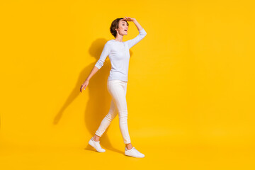 Fototapeta na wymiar Full length photo of friendly cute young woman wear white shirt walking looking far away isolated yellow color background