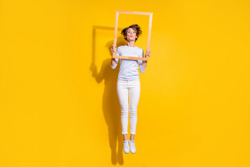 Photo of crazy lady jump send air kiss hold wooden frame wear white shirt trousers footwear isolated yellow color background