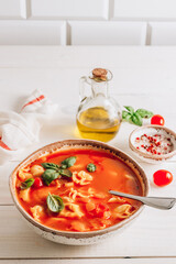Tomato soup with tortellini in white bowl on white wooden table.