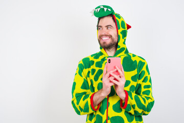 Fototapeta premium young caucasian man wearing a pajama standing against white background hold telephone hands read good youth news look empty space advert