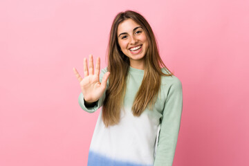 Young woman over isolated pink background saluting with hand with happy expression