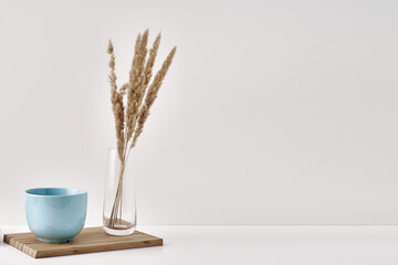 A transparent vase with dry branches and mug on a white background. Minimalism, eco-materials in the interior decor. Copy space, mock up.