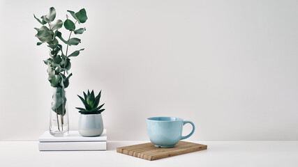 A mug, a stack of books, a wooden board and a transparent vase with eucalyptus branches. Eco-friendly materials in interior decor, minimalism. Copy space, mock up