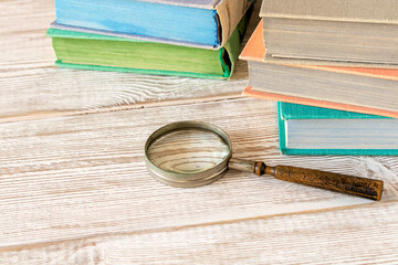 An old magnifying glass and a stack of books on a wooden table. The concept of getting knowledge...