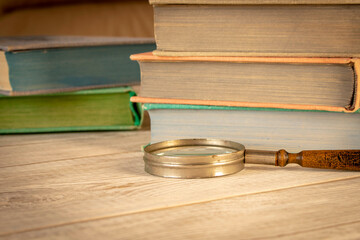 An old magnifying glass and a stack of books on a wooden table. The concept of getting knowledge...