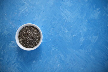 Chia seeds are organic food for a healthy diet. In a round bowl. The blue background is painted with oil paints.