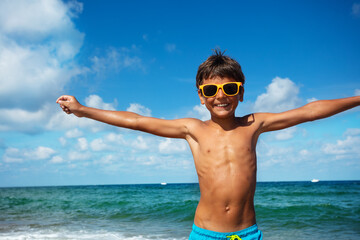 Portrait of a happy relaxed boy in sunglasses with big smile lift hands standing near sea © Sergey Novikov