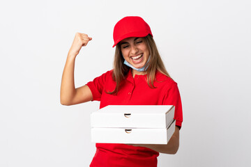 Pizza delivery woman holding a pizza and protecting from the coronavirus with a mask over isolated white wall celebrating a victory