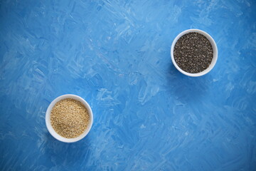 Quinoa and chia seeds are organic food for a healthy diet. In a round bowl. Two white cups. The blue texture is painted with blue oil paints