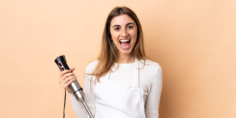 Woman using hand blender over isolated background with surprise facial expression