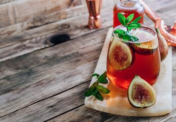Cold lemonade cocktail with figs on rustic wooden background
