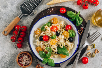 Heart pasta salad with colorful tomatoes, olives, parmesan and basil leaves