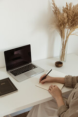 Working at home concept. Aesthetic minimalist workspace background. Young woman write notes in...