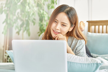 Naklejka premium 동양인 한국인 아름다운 여성 모델 침대위에서 노트북을 보며 휴식, 쇼핑, 화상채팅 