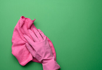 female hand in a pink rubber glove holds a pink cleaning rag on a purple background, close up