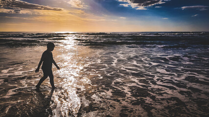 Fototapeta premium Silhouette of child walking on the beach early in the morning as the sun rises. Sunshine Coast, Queensland Australia