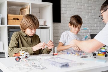 Young boys and teacher having fun constructing robot cars at the workshop