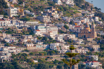 Fototapeta na wymiar Beautiful Church with a golden dome and green trees in Amalfi on hills, Campania, Italy.