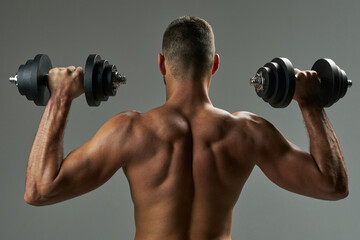 Fototapeta na wymiar Adorable strong bodybuilder doing building up muscles with dumbbells in room indoors