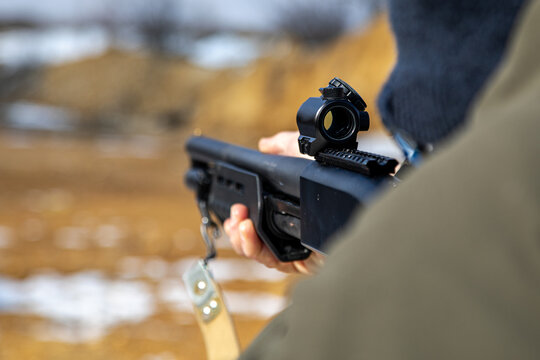 
Shooter aiming with a collimator from a shotgun at a shooting range in the cold season, close-up, soft focus