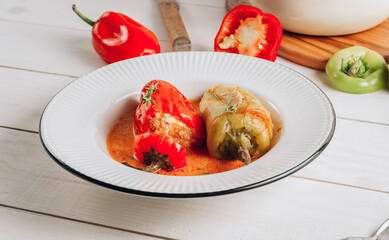 Pepper stuffed with minced chicken meat and rice in a white plate on a white wooden table.