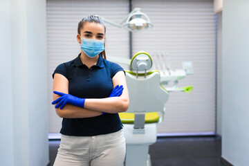 Fototapeta na wymiar Young female dentist doctor in mask stands in the office with his arms crossed