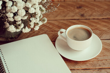 Obraz na płótnie Canvas Morning cup of coffee with paper notepad on wooden table. Morning coffee mug for breakfast, empty notebook with vintage filter effect. copy space. planner mockup. Cozy work space