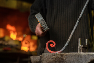 The blacksmith twists the spiral with a sledgehammer, placing a red-hot iron blank on the anvil. Work in the forge