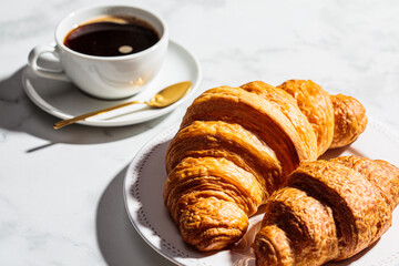 Fresh breakfast croissants with coffee on white marble background.