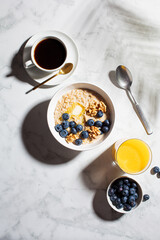 Breakfast flat lay. Oatmeal bowl with berries and nuts, cup of coffee and glass of orange juice on white marble background.