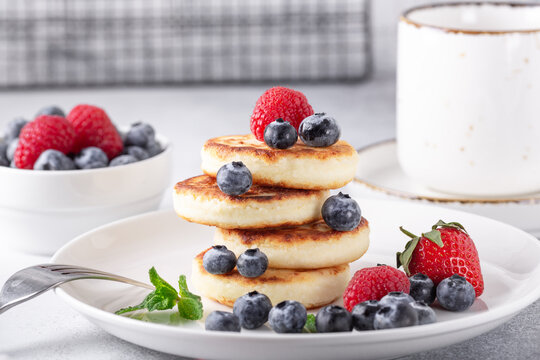 Stack of cheese pancakes with fresh berries, cup of coffee on the table. Tasty breakfast food - Image