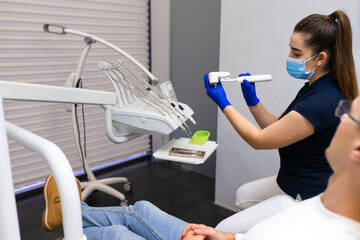 Dentist hygienist using the example of artificial jaw shows how to properly brush your teeth with electric brush