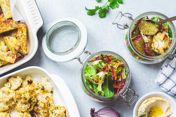 Cooking healthy food concept. Baked cauliflower, sweet potato, hummus and salad in jars on gray background, top view. Cooking food for the week.
