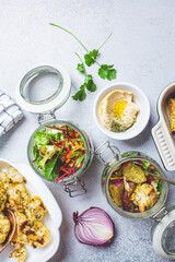 Cooking healthy food concept. Baked cauliflower, sweet potato, hummus and salad in jars on gray background, top view. Cooking food for the week.