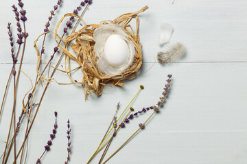 an egg in a nest of straw and feathers, on light wooden planks with lavender flowers. The layout of the space