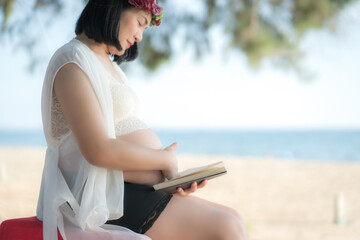Obraz premium Asian Pregnant woman reading a book with copy space. (Vintage tone) at beach .Young pregnant woman .