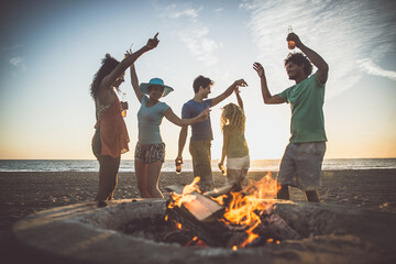 Group of friends having fun on the beach making a bonefire. People spending time together in...