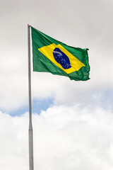 Bandeira do Brasil hasteada, balançando ao vento com o céu e nuvens ao fundo.