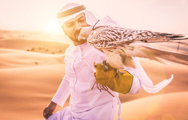 Arabic man with traditional emirates clothes walking in the desert with his falcon bird