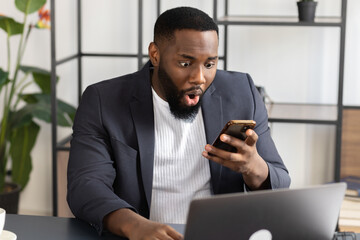 Young african american businessman or student reading unexpected good news on smartphone