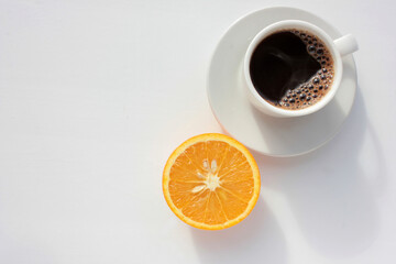 Cup of coffee and half of orange fruit on white background. Top view, copy space. Morning espresso...