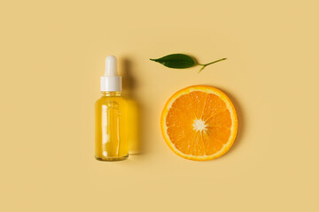 Bottle of serum of vitamin c and orange and green leaf flat lay on yellow background