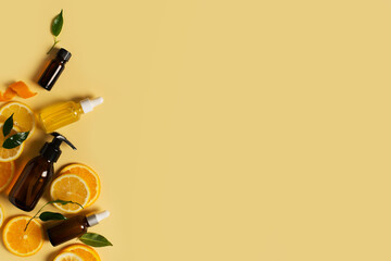 Bottles of serum of vitamin c and orange, lemon and green leaf flat lay on yellow background