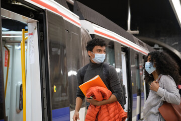 Young latin couple wearing protective face mask going inside the train, metro, subway. New normal...
