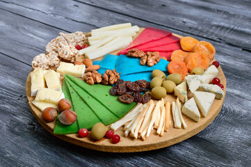 Different kinds of cheeses, dried apricots, whole-grain breads, nuts, olives, capers on a wooden board. Cheese board, snacks.