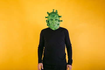 Person disguised as coronavirus with latex mask - covid-19 virus on yellow background. Coronavirus...